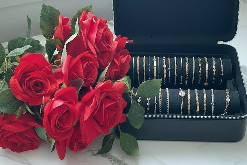 Open jewelry box with bracelets and a bouquet of red roses on a marble surface