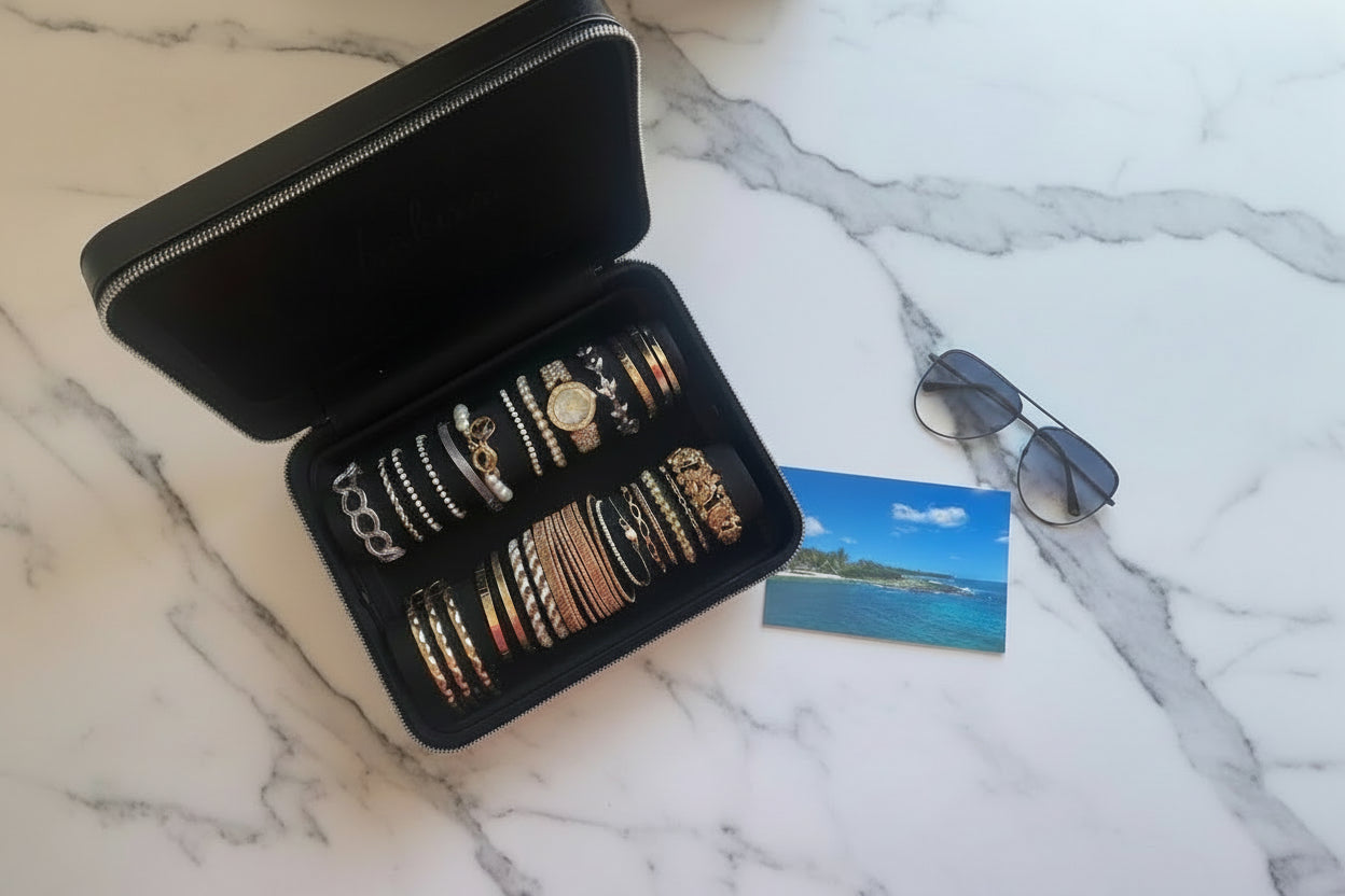 Black jewelry case with bracelets, sunglasses, and a tropical theme photo on a marble surface